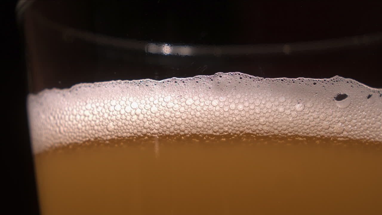 detalle de primer plano: burbujas burbujean y explotan en la cabeza de un vaso de cerveza lager