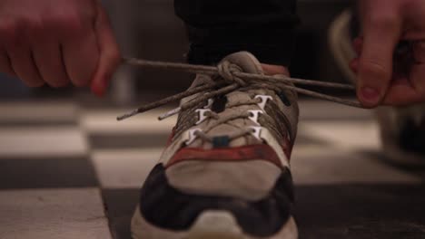 close-up of hands tying the laces on a worn sneaker, indoor lighting