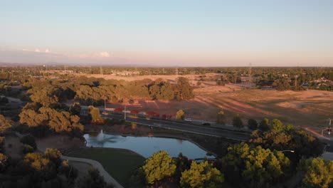 aerial-view-of-suburban-city-with-trees,-pond,-field-and-road