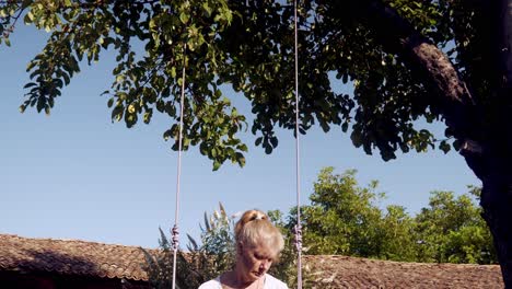 push shot towards woman sitting quietly on garden swing under apple tree