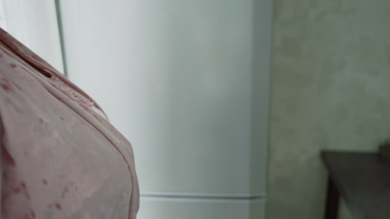 close up of girl tightening backpack strap over shoulder in bright kitchen during morning routine, preparing for school day with focus on hand grip and bag detail, emphasizing daily preparation moment