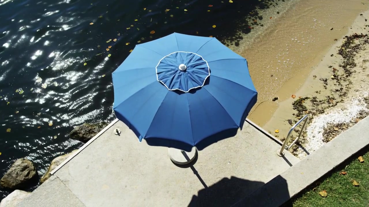 Iniziando con una persona che cammina brevemente in alto a destra, un ombrellone blu posizionato su un patio in cemento con una scala.