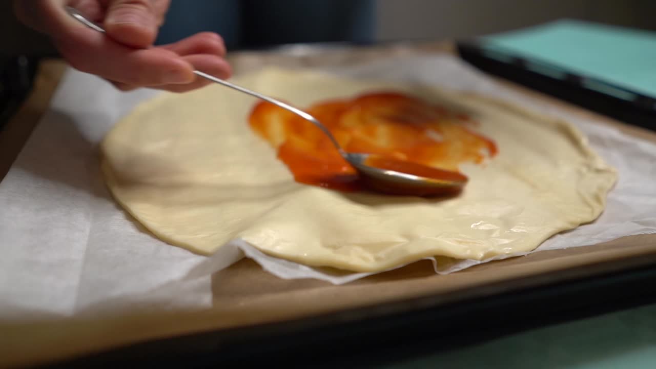 mujer esparciendo tomate en masa de pizza en bandeja y en mesa turquesa