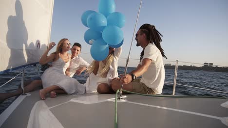 four friends having relaxing cruise on the yacht while lying on a bow of the boat. they enjoying the moment - girl in a white waving the balloones, celebating. slow motion. sunny day spending outdoors