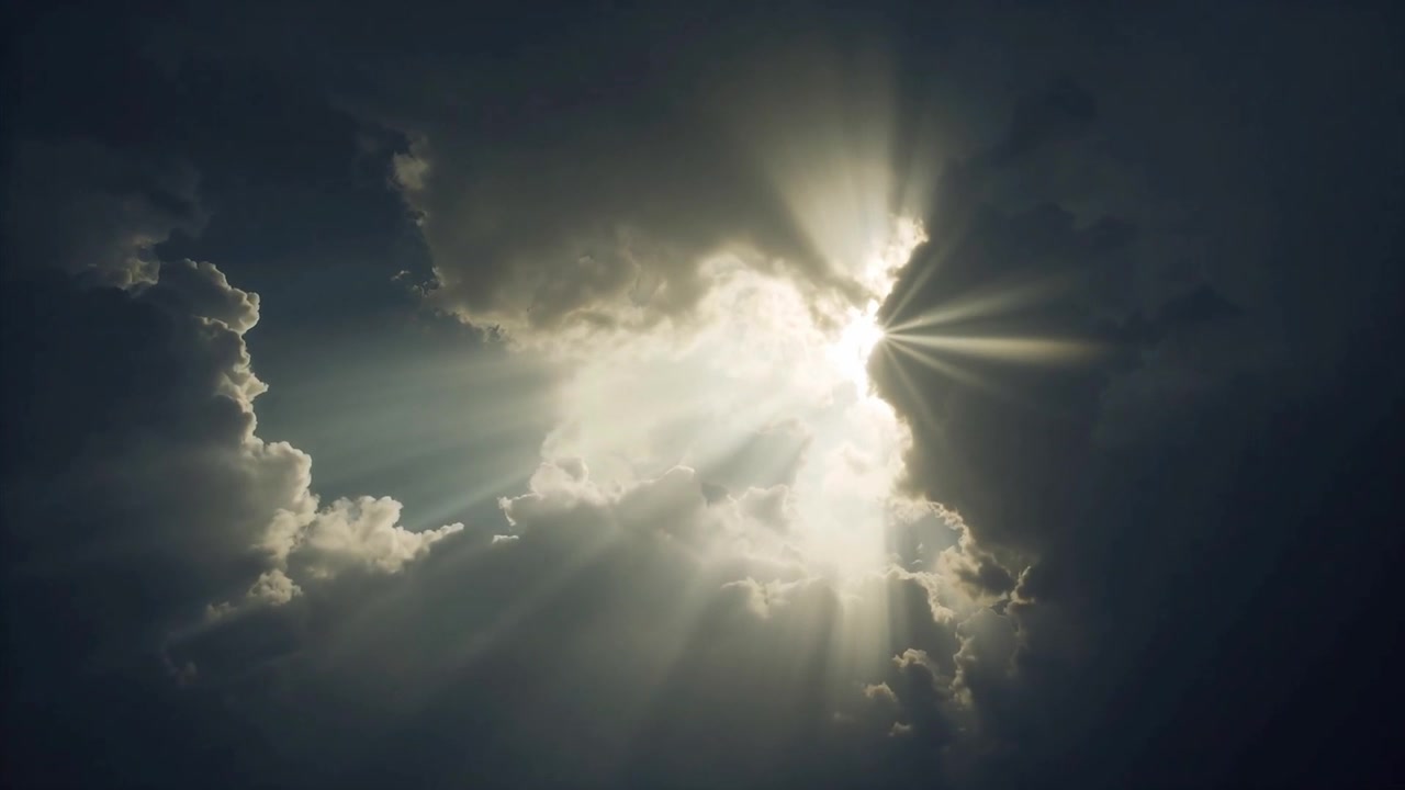 Una nuvola luminosa che si apre inviando raggi di sole attraverso un cielo tempestoso, illuminando i bordi delle nuvole.
