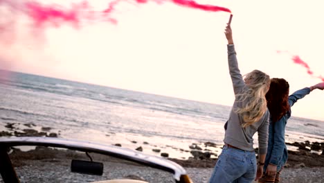 friends with convertible car celebrating with smoke bombs at beach