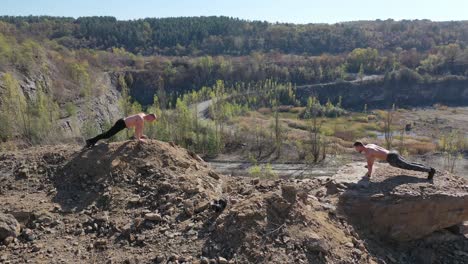 shirtless sportsmen training on the nature background. two young athletes doing push ups in the mountainous area in summer day. aerial view.