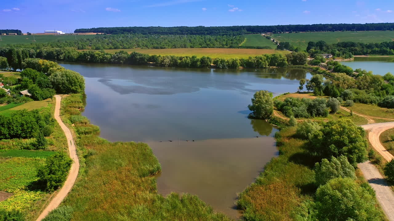 Rising over the beautiful small river in the countryside crossed by the road. Green fields and forests around the river. Top view.