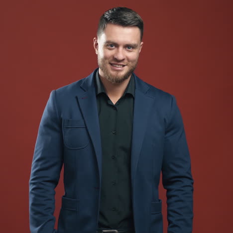 handsome man in stylish suit. portrait of young businessman in the red studio. smiling bearded man in black shirt and blue jacket looking at camera.
