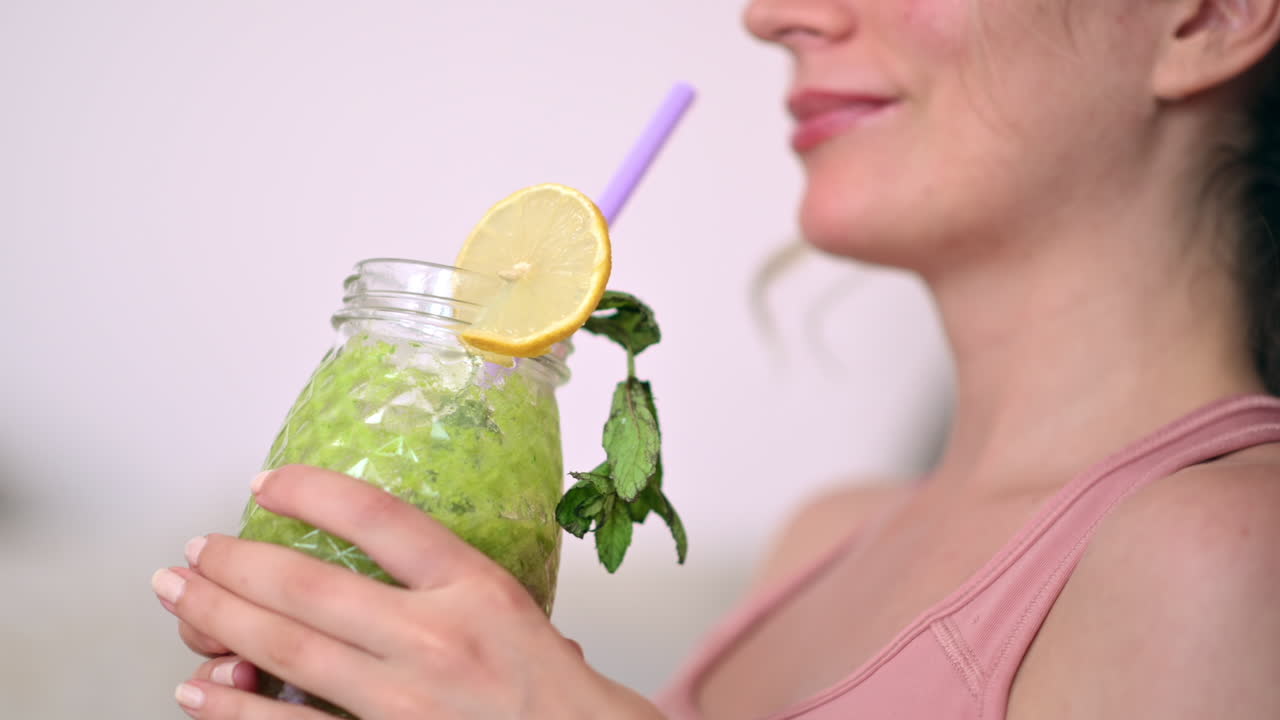Close up of a woman drinking a green juice while sitting on a couch