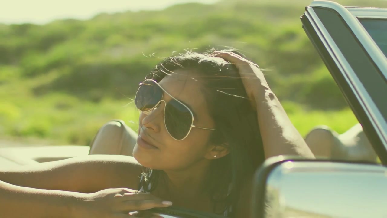 Woman passenger sweeping hair toward sun in travel convertible, camera shifting revealing confetti