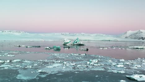 cracked ice and icebergs in jokulsarlon glacial lake with pink sky at sunrise in iceland