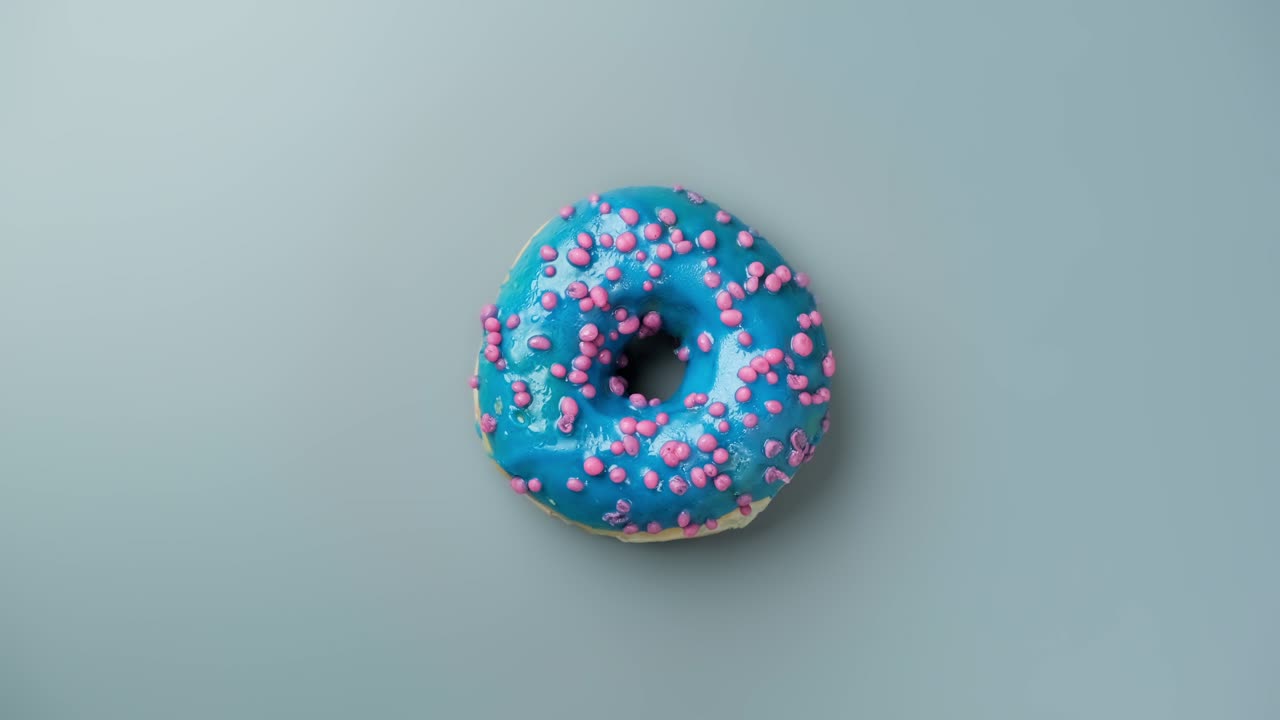 Blue frosting donut with sprinkles at light blue background. Sweet dessert.