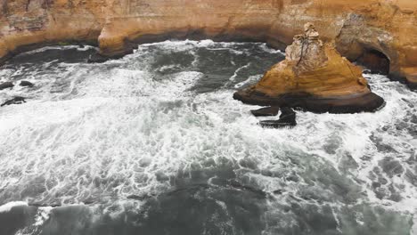 tilt up aerial shot, from the surface of the ocean to people standing at he edge of the cliff at the ocean coastline