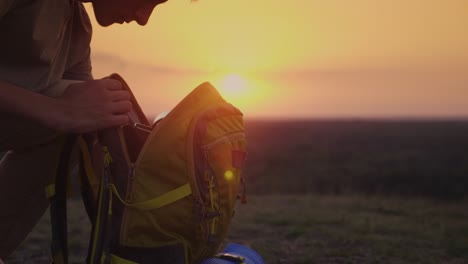 a man is packing his backpack at sunset. preparing for a trip or trekking