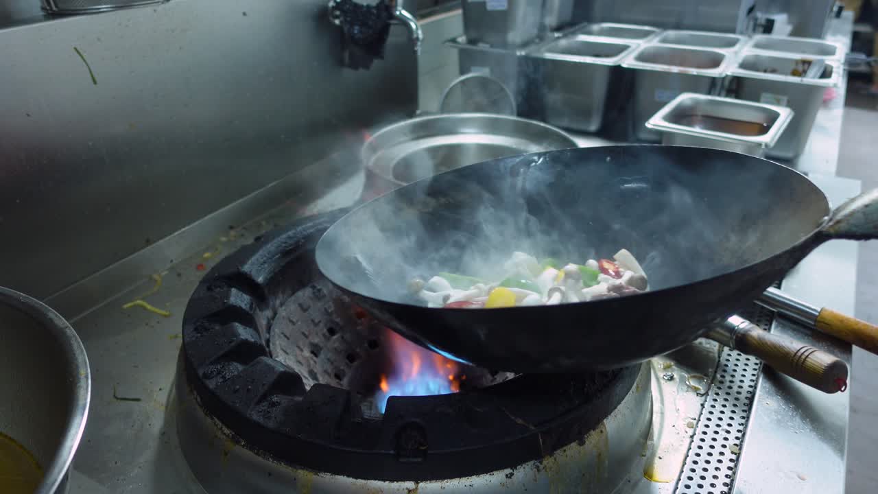 Uno chef aggiunge olio da cucina nel wok prima di mettere gli ingredienti misti per il manzo saltato in padella in una cucina commerciale. Scatto ravvicinato.