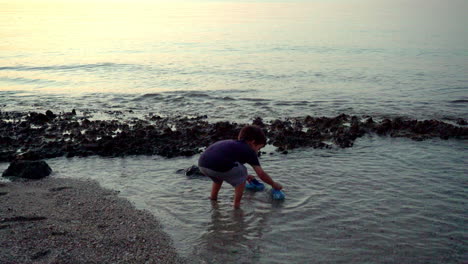 artistic shot of caucasian boy, wetting his feet, and playing at the beach, late evening with beautiful colours 4k