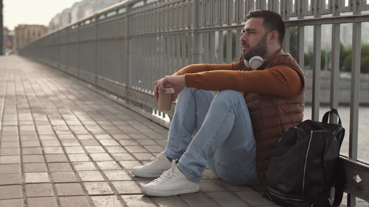Man Sitting on Sidewalk by Fence