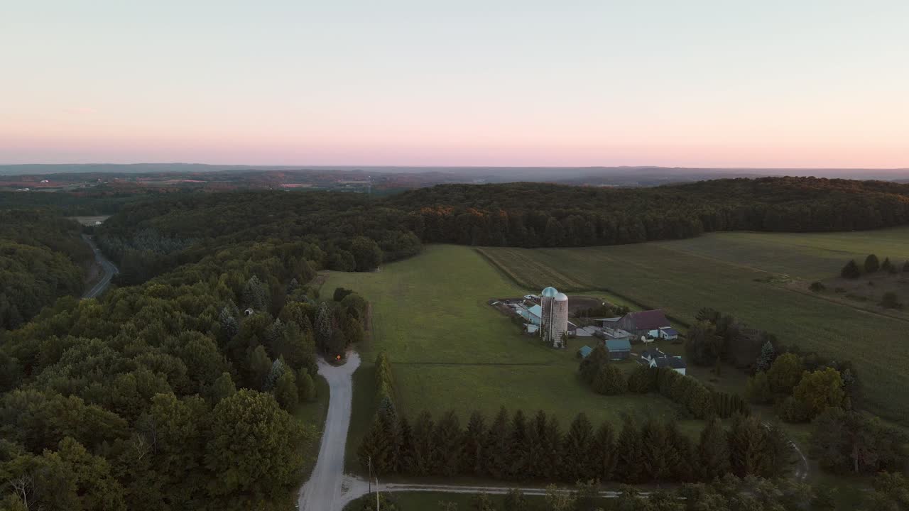 Laaja ja hidas ilmasta kiertävä kuva maatilasta siiloineen Pohjois-Michiganin kumpuilevilla kukkuloilla auringonlaskun aikaan.