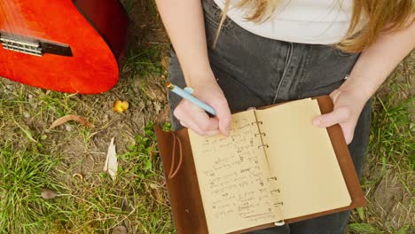 Female-guitarist-composer-writes-chords-lyrics-song-book-top-down-shot