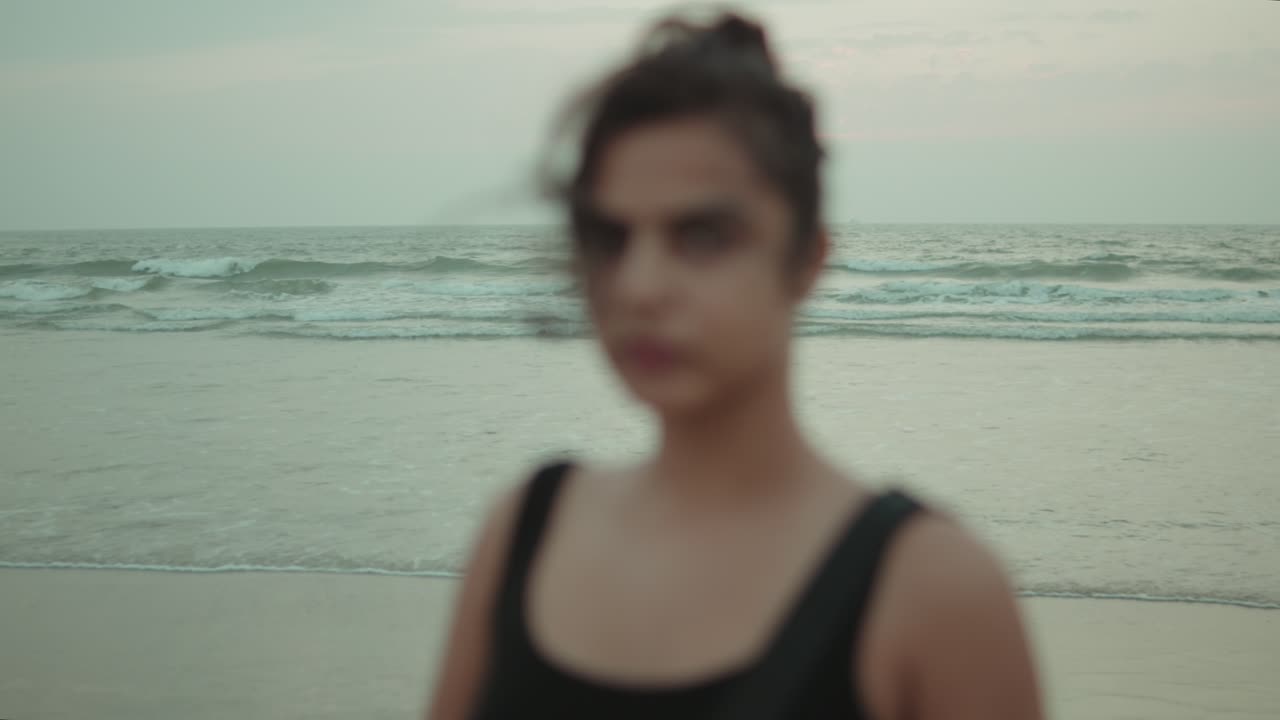 A blurred silhouette of a woman in black stands against the waves at Utorda Beach, South Goa, during dusk