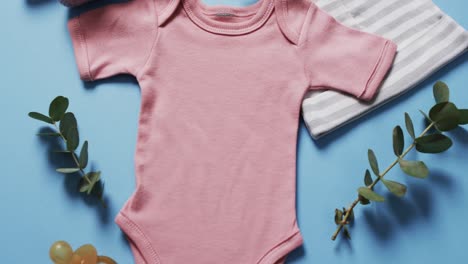 Video-of-pink-baby-grow,-booties-and-hat-with-copy-space-on-blue-background