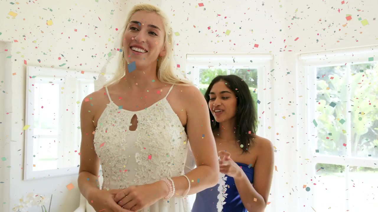 Vidéo verticale : Mariée ajustant ses cheveux et son voile, amie arrangeant une guirlande dans la pièce, confettis tombant.