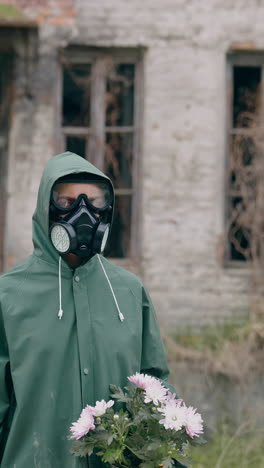 survivor holding flowers on ruined building background. person in chemical safety suit and respirator standing with flowers in hands in abandoned place. chemical attack. vertical video