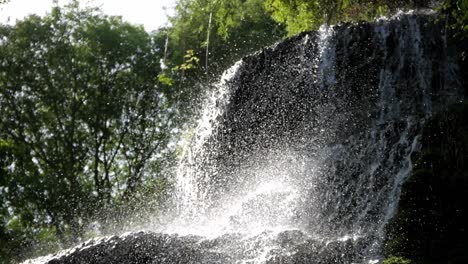 beautiful water flow pouring down rock fall and splashing on sunlight. tall trees foliage background. forest scenery. monasterio de piedra, zaragoza, spain
