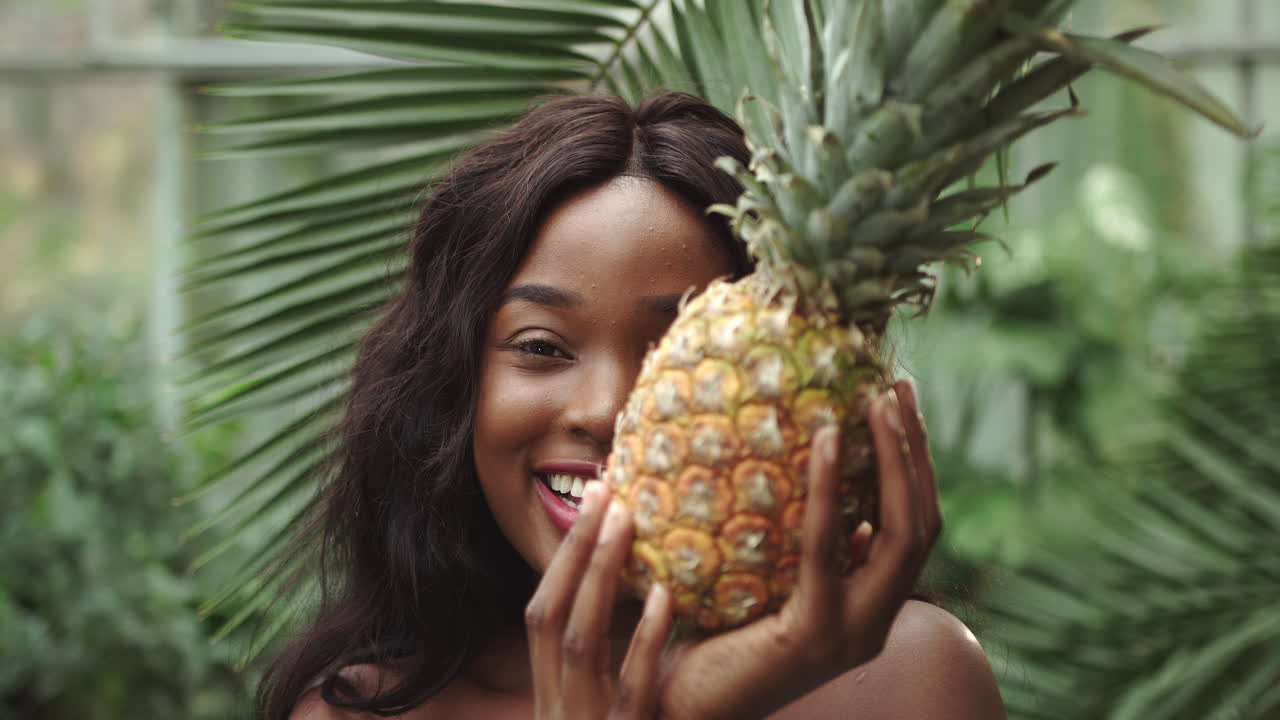 Young beautiful girl with natural makeup holds a pineapple in her hands and smiles at the camera