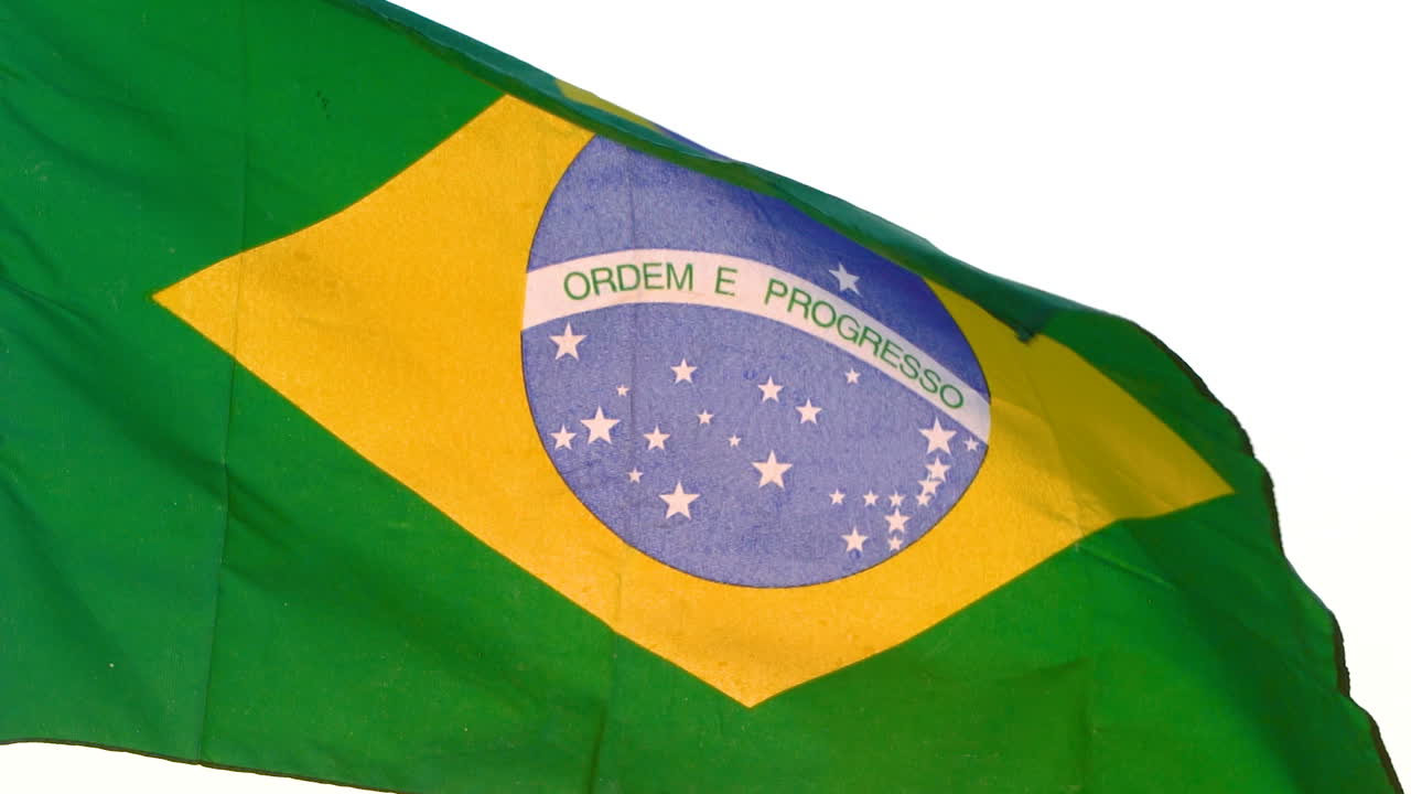 Bandeira do Brasil a tremular sobre fundo branco.