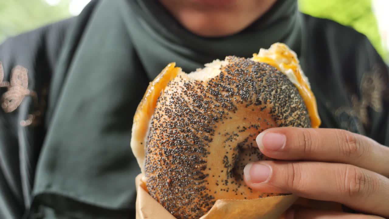 mujer comiendo un sándwich de bagel de semillas de amapola
