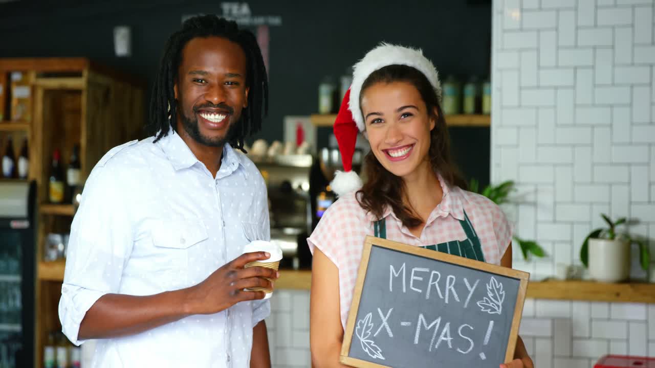 Porträt einer Kellnerin und eines Kollegen, die mit einer Frohe-Weihnachten-Tafel stehen