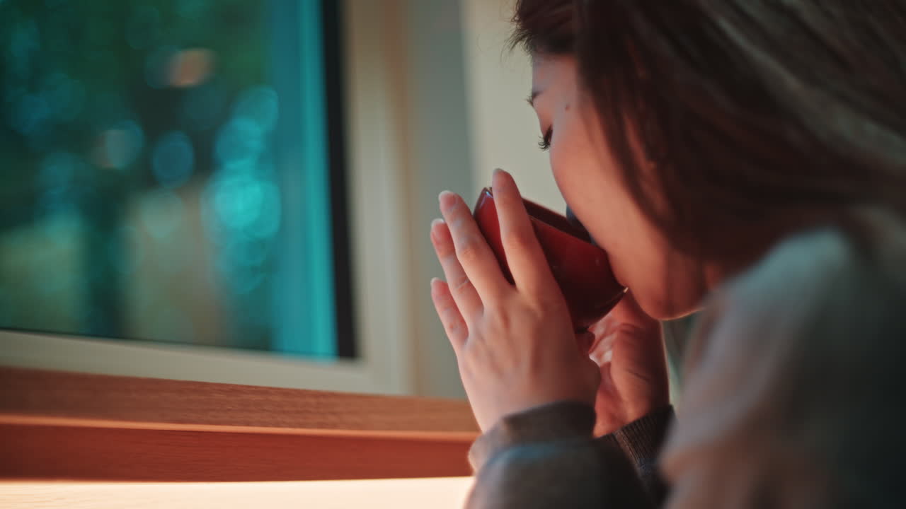 Woman drinking from cup by the window