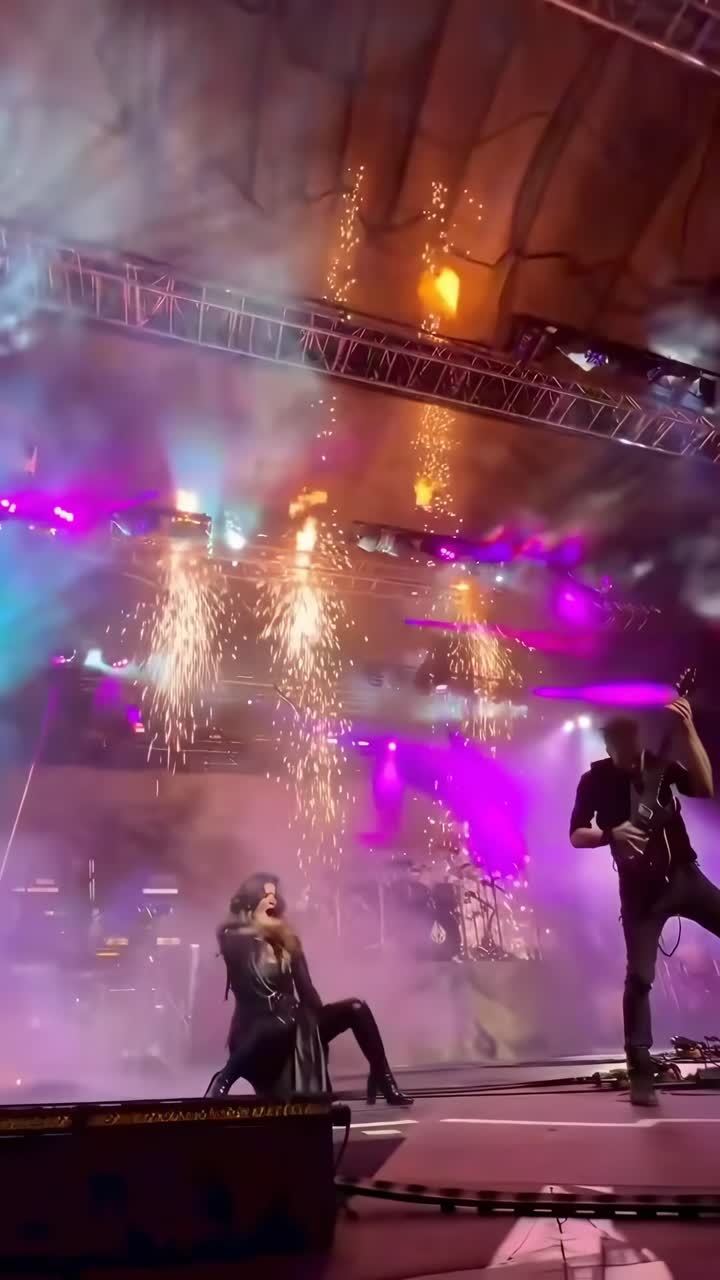 Video dinámico de escenario con una toma en ángulo bajo de una banda de rock, luces vibrantes y fuegos artificiales.