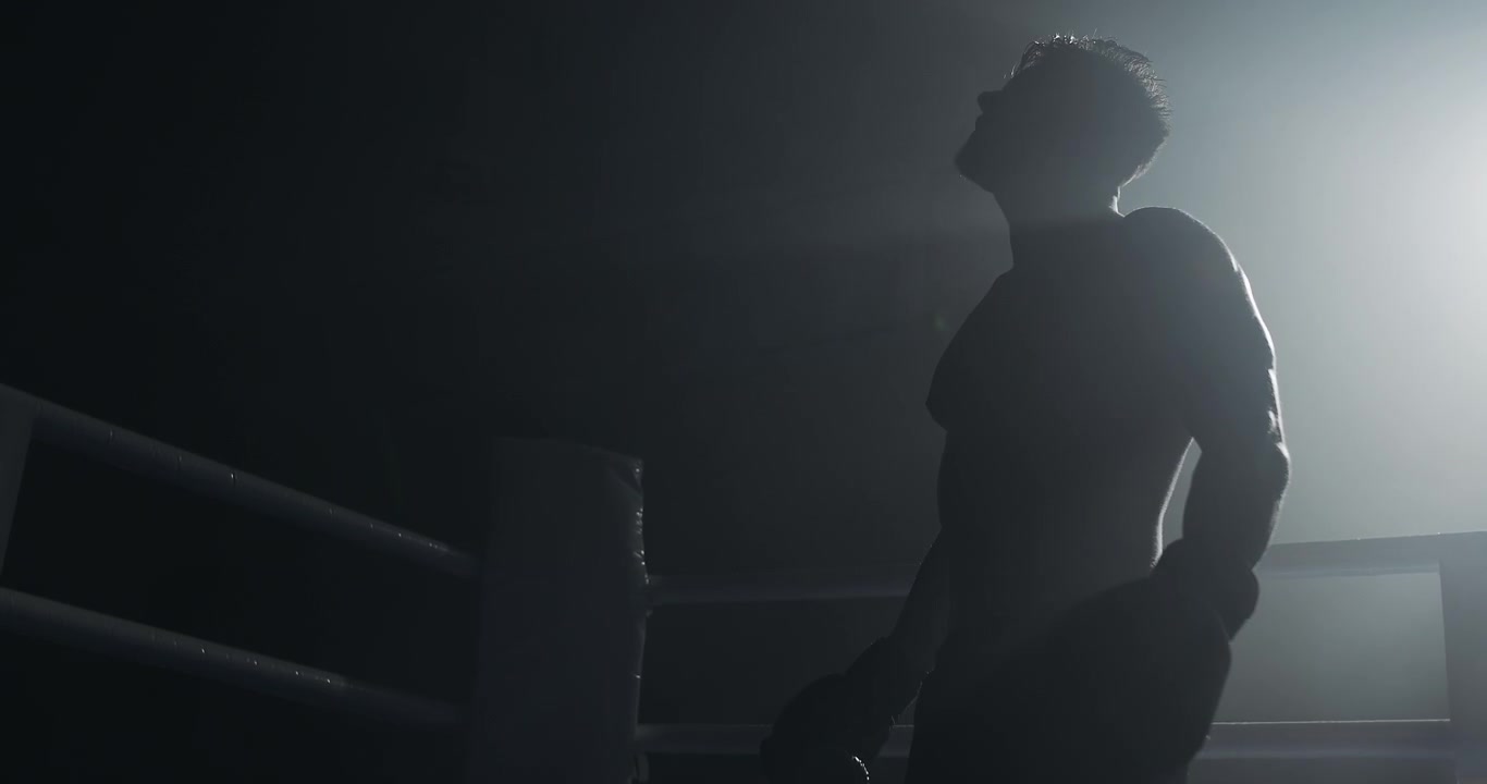Silhouette of a Boxer Putting on Gloves in a Dark Ring