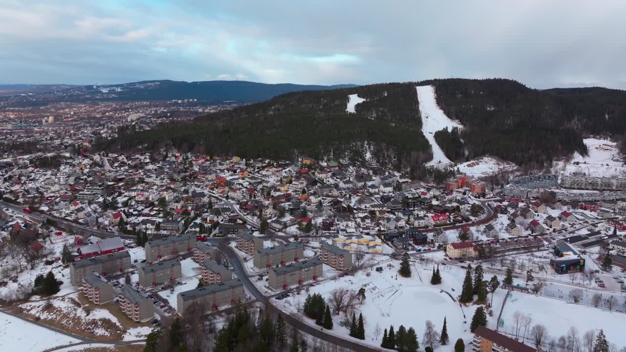 Skikurs skisenter Bjerke Arvoll Tonsengagen Oslo Norge Norway aerial drone cold cloudy winter day gray skies city neighborhood buildings landscape Arctic circle snowing forward pan up motion
