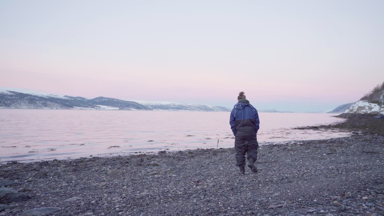 un hombre vestido de invierno con su perro caminando por la costa de guijarros cerca de vanvikan, indre fosen, noruega