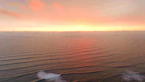 high vivid sunset drone view over ocean as swell rolls in toward coastline