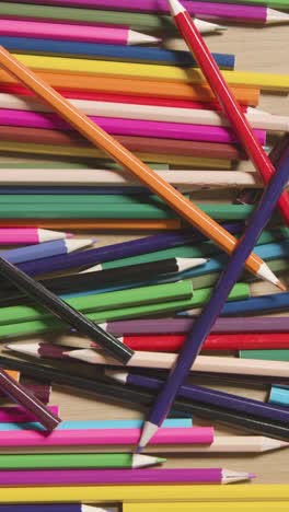 video vertical de lápices de colores aleatorios sobre un fondo de madera con una persona que recoge un lápiz púrpura