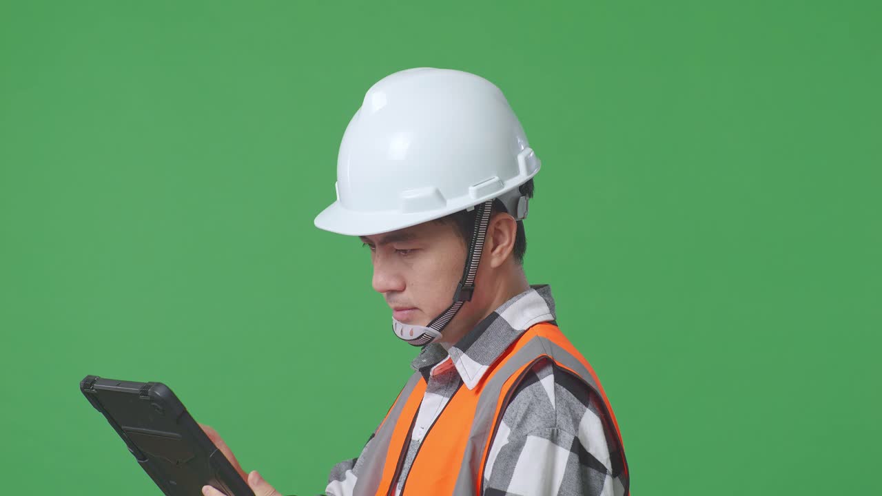 Close Up Side View Of Asian Male Engineer With Safety Helmet Working On A Tablet While Standing In The Green Screen Background Studio