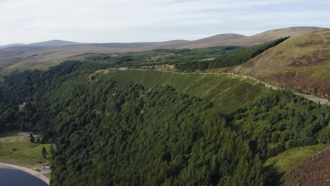 vista aérea de una larga y sinuosa carretera de montaña vacía en las montañas wicklow con lough tay en la vista en un día soleado