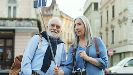 happy senior couple standing outdoors with a smartphone and a selfie stick