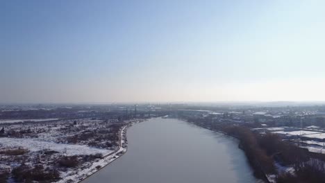 Flying-upwards-above-a-perfect-frozen-lake-and-a-snowy-background-with-a-clear-sky