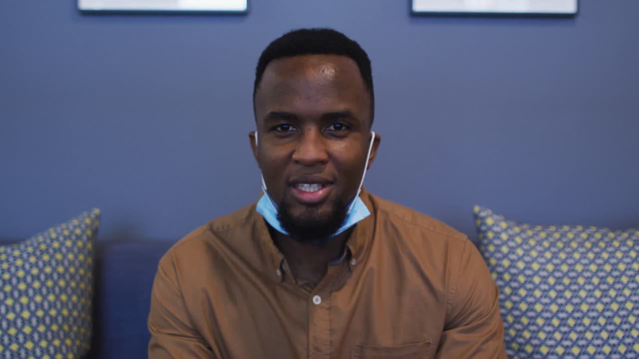 Portrait of african american man face mask around his neck talking and waving looking at camera