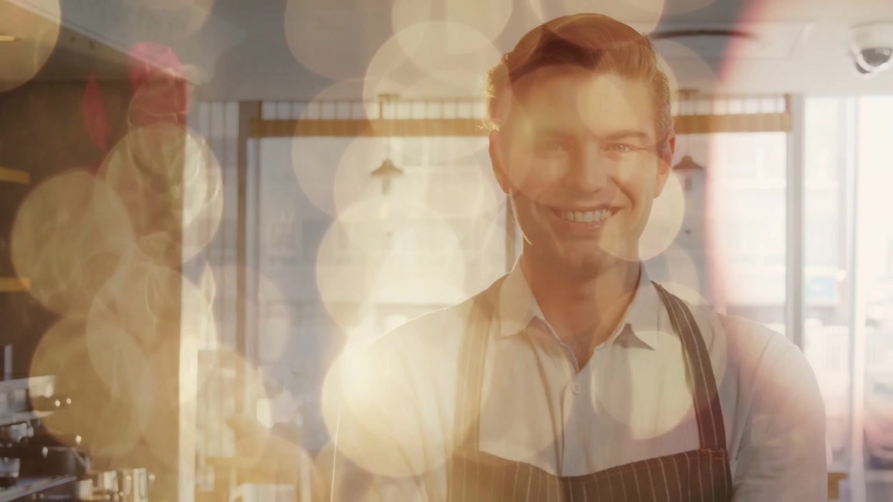 Ein männlicher Barista steht lächelnd hinter der Theke, während sich ein Bokeh-Effekt lichtet und das Café enthüllt.