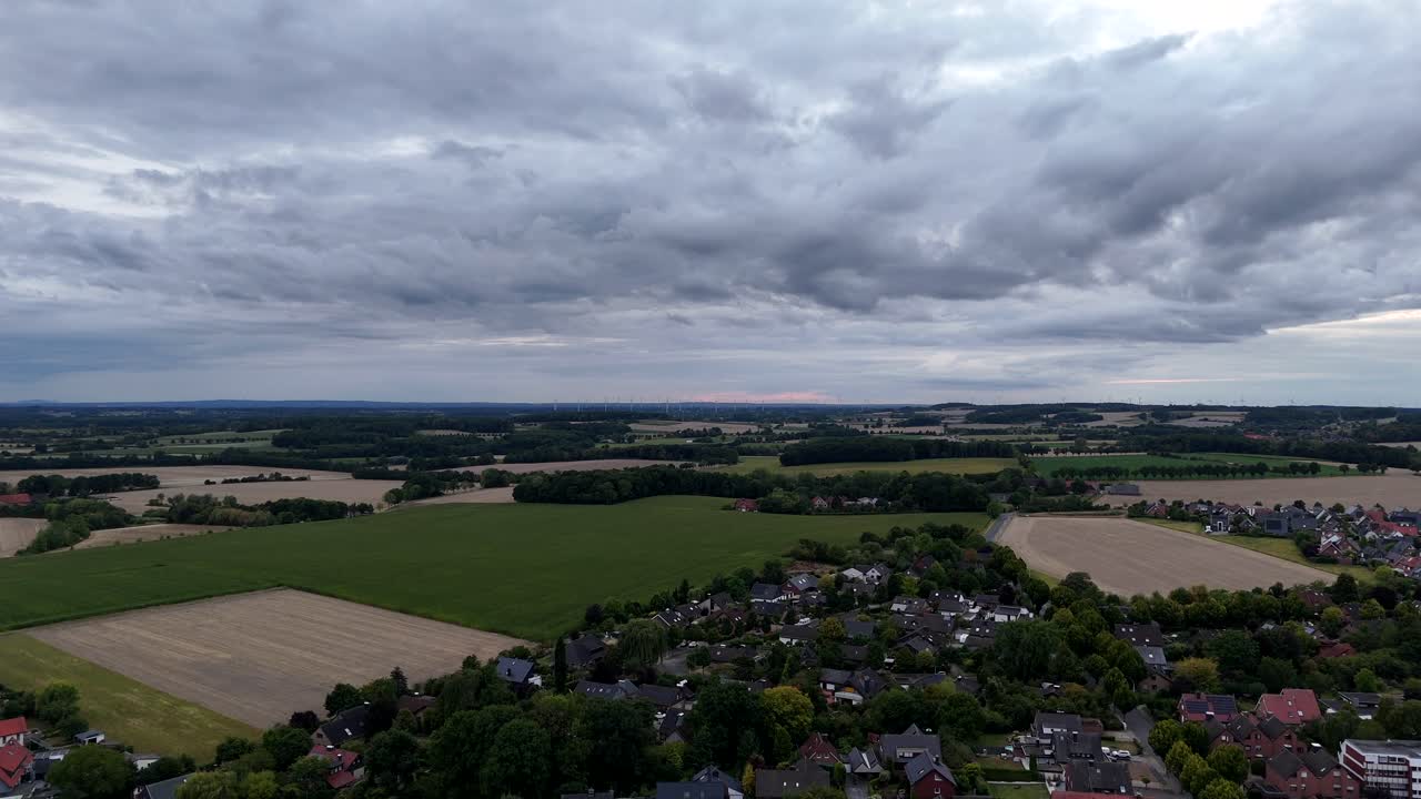 American cityscape during cloudy summer day. Aerial rising wide shot. Single family houses bordering to agricultural farm fields in USA. Wheat and green corns growing in August