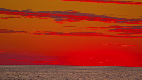 time-lapse shot of deep red and orange sunset over a calm sea