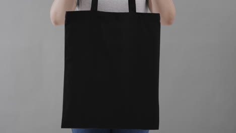 mujer caucásica con camiseta blanca sosteniendo una bolsa negra sobre un fondo gris, espacio de copia, cámara lenta