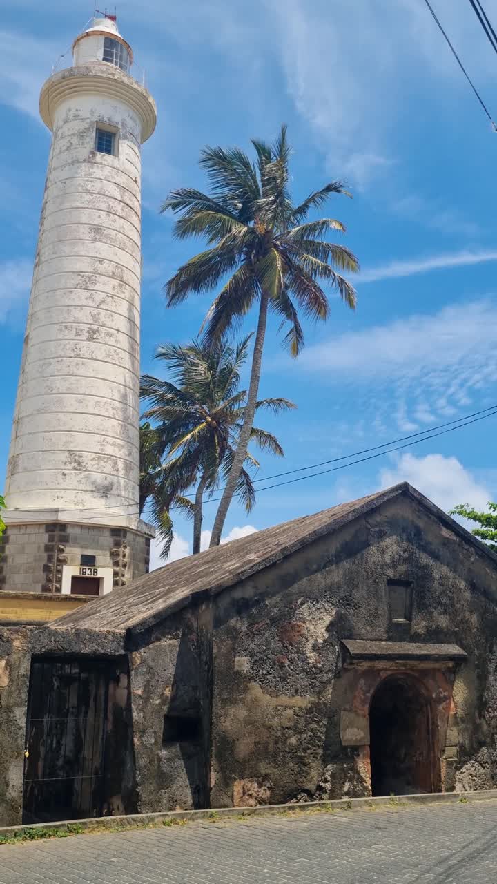 Vista verticale del faro di Galle in Sri Lanka sotto un cielo azzurro limpido, con palme che ondeggiano al vento costiero, che mette in risalto l'iconico punto di riferimento sul mare